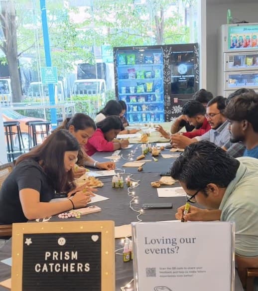 Team painting prism catchers at a long workshop table